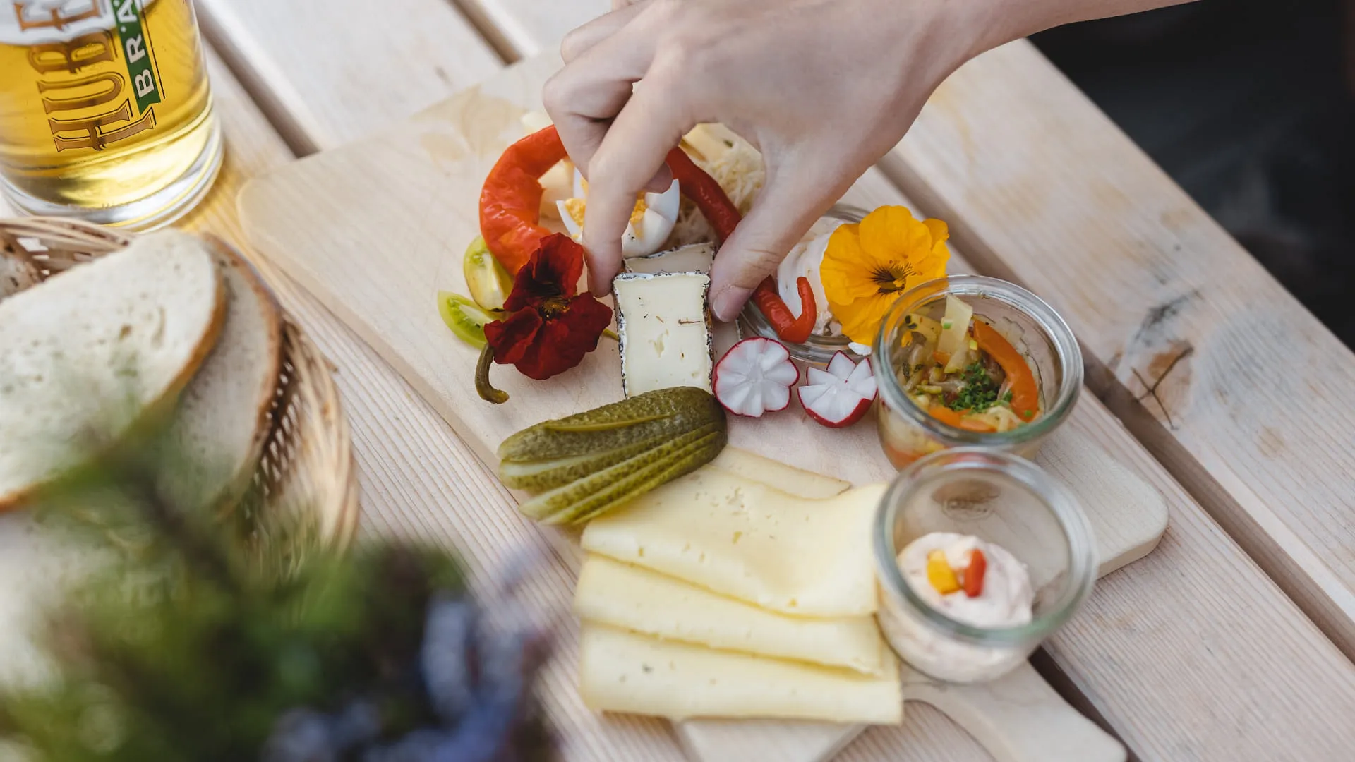 Hände bereiten eine kulinarische Platte mit Käse, Gemüse und Dips vor.