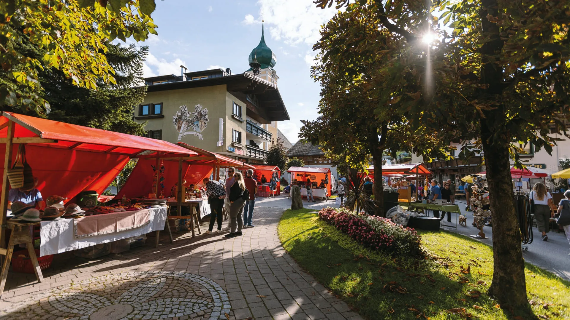 Lebhafter Marktplatz im Sommer mit roten Ständen und Blick auf einen historischen Gebäudeturm.