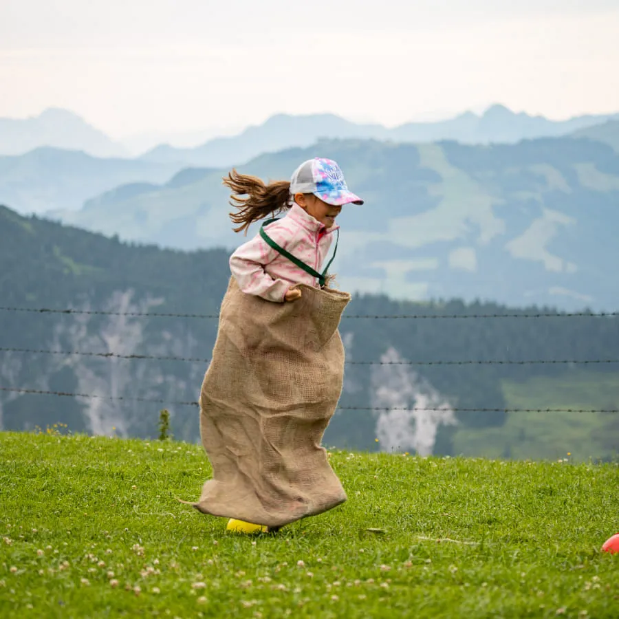 Mädchen springt in einem Sack auf einer Wiese im Brixental