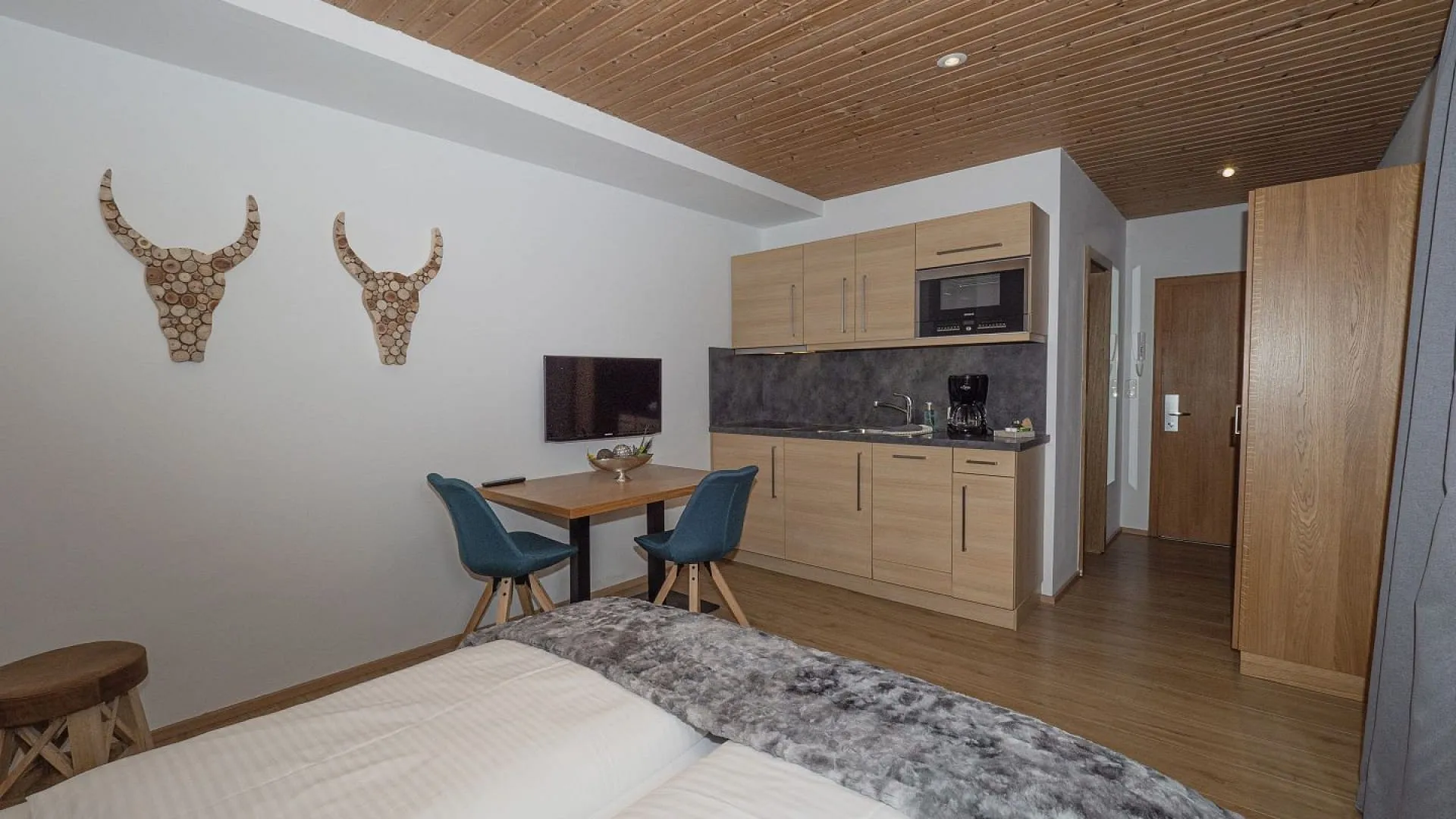 Helles Zimmer mit Holzdecke, Küchenzeile, Tisch und zwei Stühlen.