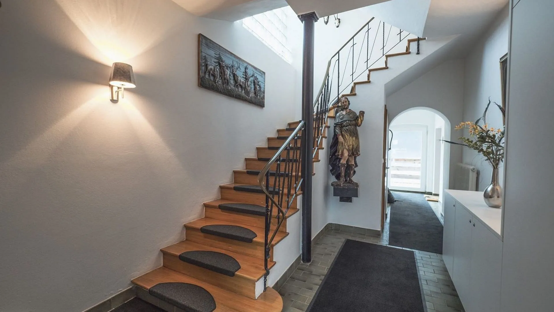 Heller Eingangsbereich mit Treppe, Skulptur und Wandkunst.