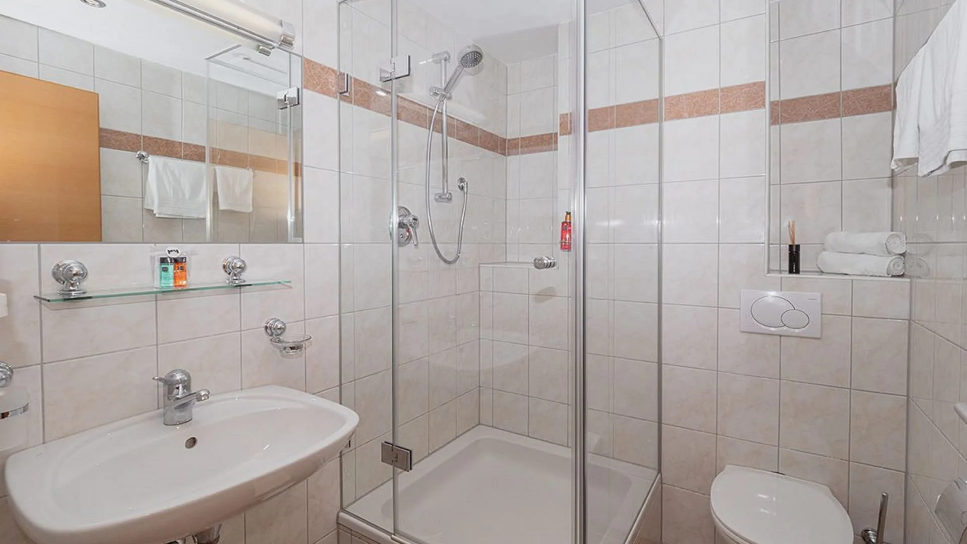 Badezimmer mit Dusche, Waschbecken und WC, helle Fliesen und Holzdetails